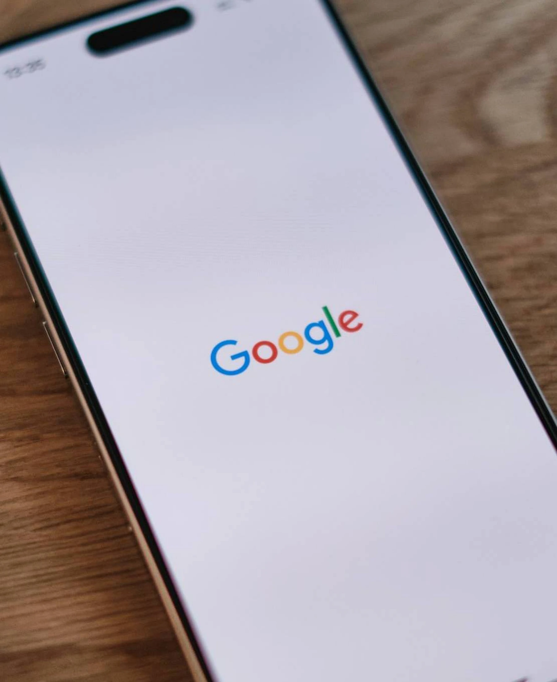 Bild eines Smartphones, das auf einem Holztisch liegt. Das Display zeigt das Wort Google in den typisch bunten Buchstaben, die Google nutzt.
